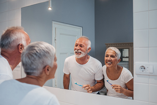 Elderly couple smiling and brushing their teeth in the bathroom mirror
