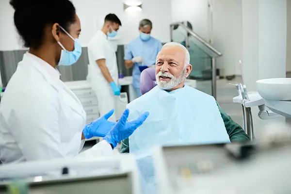 Older patient sitting in dental chair calmly discussing his oral health with his female dentist at Cascade Dental in Medford, OR