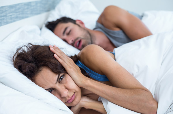 Woman covering ears while husband snores should seek help at Cascade Dental in Medford, OR